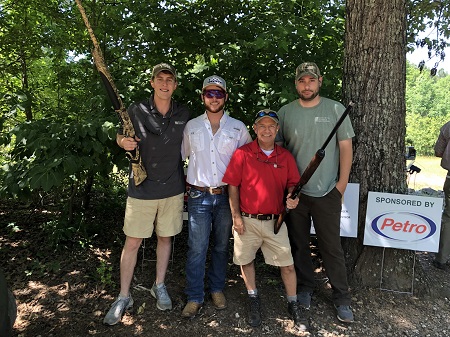 Group of four men holding rifles posing in front of some trees