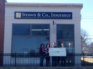 Strawn & Co agents pose with check for facade grant program in front of the strawn & co office