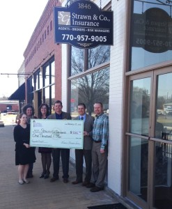 Strawn & Co agents pose with check for facade grant program in front of the strawn & Co office sign